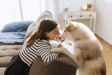 Lächelndes Mädchen mit geschlossenen Augen, das sich mit einem Siberian Husky zu Hause auf das Sofa lehnt - MIMFF00580