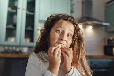 Mädchen mit braunem Haar isst Mandarine, während sie am Esstisch in der Küche sitzt - MIMFF00589