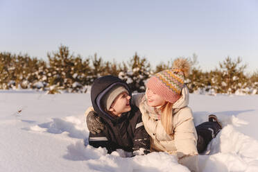 Verspielte Geschwister auf Schnee liegend gegen den Himmel im Winter - EYAF01520