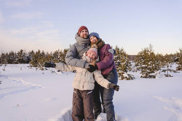 Glückliche Familie in warmer Kleidung auf Schnee stehend gegen den Himmel im Winter - EYAF01526