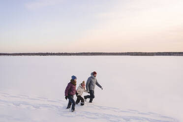 Familie, die sich an den Händen hält, während sie im Winter auf Schnee gegen den Himmel läuft - EYAF01531