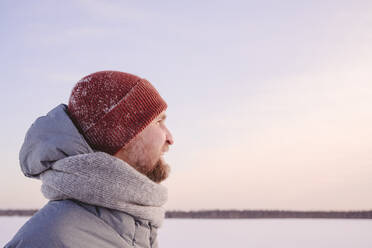 Mid adult man wearing warm clothing looking against sky during sunset - EYAF01534