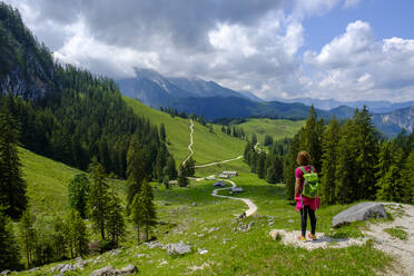 Wanderin steht mitten auf einem Wanderweg, der sich durch ein Sommertal in den Berchtesgadener Alpen schlängelt - LBF03453