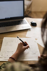 Weiblicher Schreiner mit Laptop, der am Schreibtisch in der Industrie einen Entwurf auf Papier macht - VABF04230