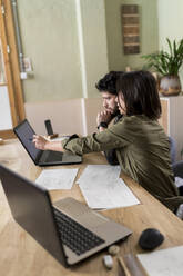 Weibliche Designerin, die einem Kollegen hilft, während sie an einem Schreibtisch in der Industrie über einen Laptop diskutiert - VABF04234
