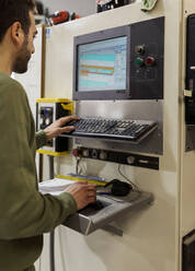 Young male carpenter operating CNC machine in workshop - VABF04243