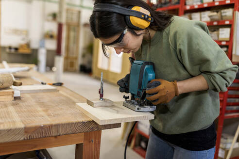 Female carpenter working with router jig at workbench in industry - VABF04267