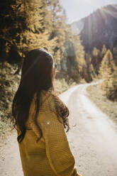 Junge Frau in Jacke schaut auf einen Weg im Wald - LHPF01398