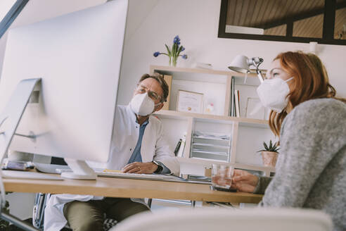 Doctor and patient wearing protective face mask using computer while sitting at doctor's office - MFF07488