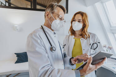 Allgemeinmediziner hält ein digitales Tablet in der Hand, während er mit einem Kollegen in der Klinik arbeitet - MFF07513