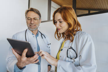 Allgemeinmediziner bei der Arbeit an einem digitalen Tablet, während er neben einem Kollegen in der Klinik steht - MFF07516