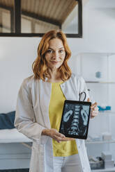 Mid adult doctor showing x-ray image on digital tablet while standing at clinic - MFF07528