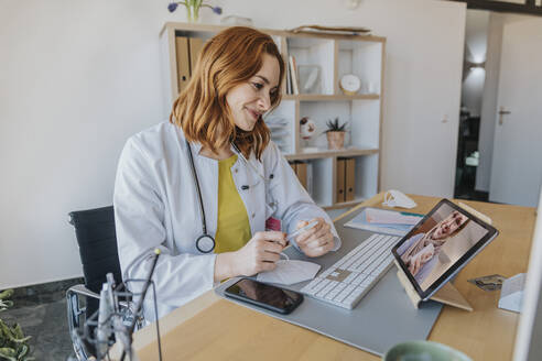 Arzt hört einem Patienten bei einem Videogespräch über ein digitales Tablet zu, während er im Büro sitzt - MFF07546