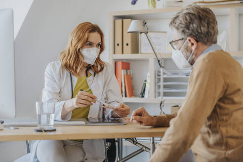 Doctor with protective face mask explaining over medication at doctor's office - MFF07568