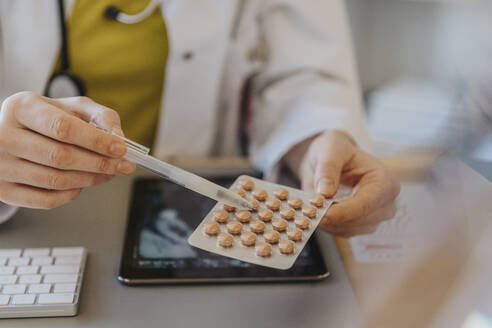 Doctor pointing at medicine while sitting by desk at clinic - MFF07569