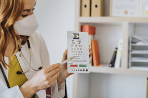 Female ophthalmologist pointing at eye chart in clinic - MFF07571