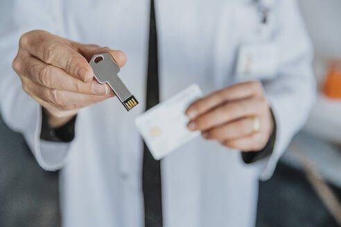 Male doctor holding USB stick while standing at clinic - MFF07579