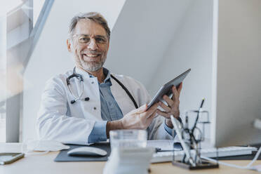 Male doctor using digital tablet while sitting at doctor's office - MFF07589