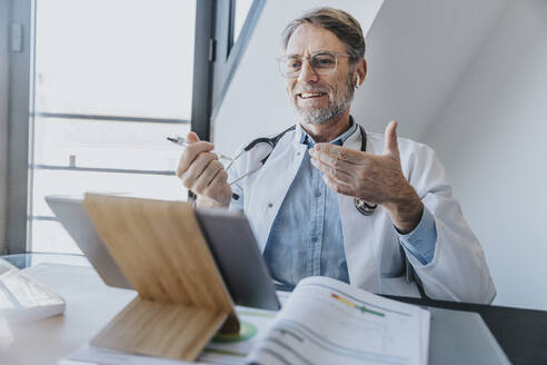 Smiling doctor discussing on video call over digital tablet while sitting at clinic - MFF07599