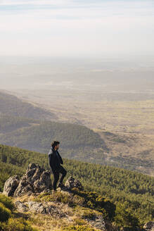 Male hiker looking at view while standing on rock at Somosierra, Madrid, Spain - RSGF00581