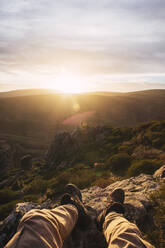 Männlicher Tourist sitzt bei Sonnenaufgang auf einem Felsen in Somosierra, Madrid, Spanien - RSGF00584