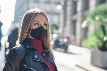Frau mit Schutzmaske schaut weg, während sie während einer Pandemie auf der Straße steht - AGOF00076
