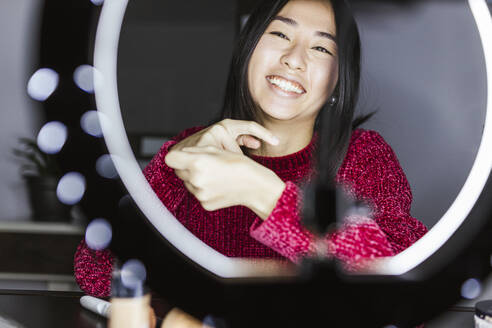 Cheerful female vlogger in front of illuminated ring light - LJF02116