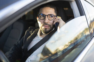 Handsome businessman looking away while talking on mobile phone in car - JCCMF01364