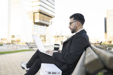 Männlicher Architekt, der einen Laptop benutzt, während er auf einer Bank in der Stadt sitzt - JCCMF01365