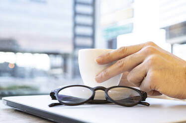 Hand hält Kaffeetasse auf Laptop in Café - JCCMF01380