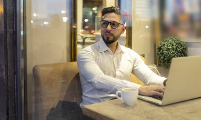 Male entrepreneur looking away while using laptop in cafe - JCCMF01381