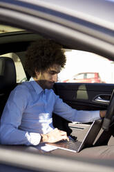 Männlicher Unternehmer, der im Auto sitzend am Laptop arbeitet - VEGF04045