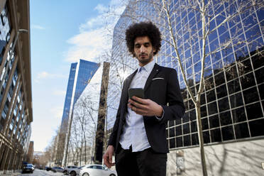 Male professional using smart phone while standing at street against building - VEGF04059