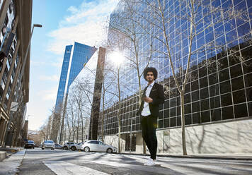 Männlicher Unternehmer, der ein Telefon in der Hand hält, während er auf dem Zebrastreifen gegen ein Gebäude läuft - VEGF04060