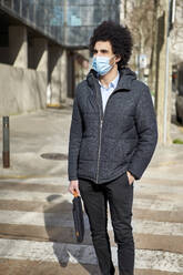 Afro man with laptop bag wearing protective face mask during pandemic - VEGF04067