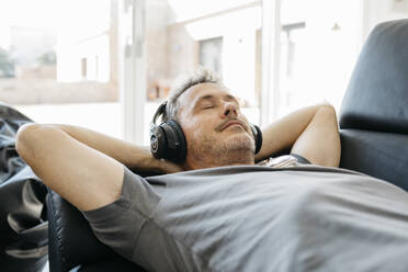 Älterer Mann hört Musik über Kopfhörer, während er sich auf dem Sofa im Wohnzimmer entspannt - JRFF05116