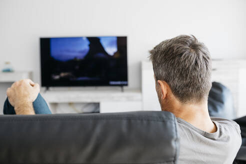 Man watching television while sitting on sofa in living room - JRFF05118