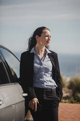 Businesswoman with hand in pocket standing by car during sunny day - DMGF00523