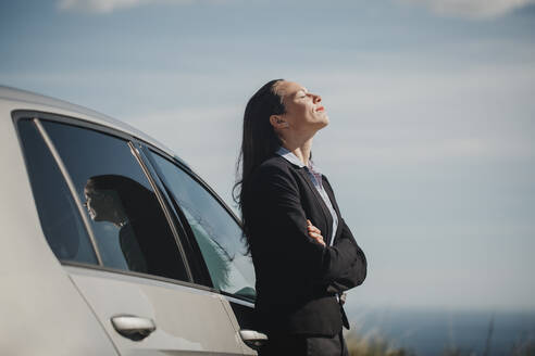 Contemplating businesswoman standing with eyes closed and arms crossed by car - DMGF00524