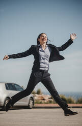 Carefree woman with arms outstretched running on footpath during sunny day - DMGF00531