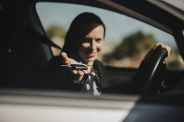 Female entrepreneur showing car key while sitting in car on sunny day - DMGF00535