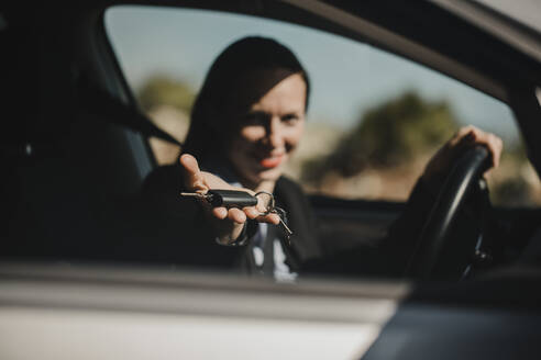 Unternehmerin zeigt Autoschlüssel, während sie an einem sonnigen Tag im Auto sitzt - DMGF00535