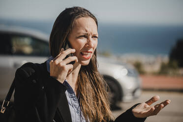 Verärgerte Geschäftsfrau, die an einem sonnigen Tag mit ihrem Mobiltelefon spricht - DMGF00541