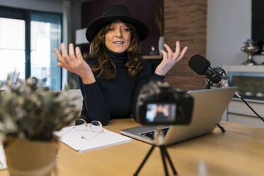 Weibliche Influencerin mit Mikrofon und Laptop im Gespräch, während sie zu Hause mit der Kamera filmt - EGAF02025
