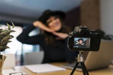 Weibliche Vloggerin gestikuliert beim Filmen mit der Kamera zu Hause - EGAF02028