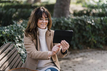Lächelnde Frau nimmt Selfie durch digitale Tablet beim Sitzen im Park - EGAF02045