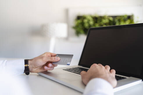 Geschäftsmann, der eine Kreditkarte hält, während er einen Laptop im Büro benutzt - DIGF14831