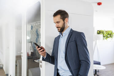 Geschäftsmann, der ein Smartphone benutzt, während er an einer Telefonzelle im Büro steht - DIGF14846