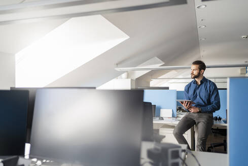 Nachdenklicher Unternehmer mit digitalem Tablet auf dem Schreibtisch im Büro - DIGF14851