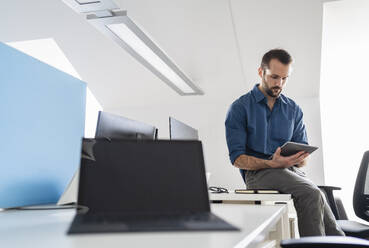 Geschäftsmann, der ein digitales Tablet benutzt, während er im Büro sitzt - DIGF14872